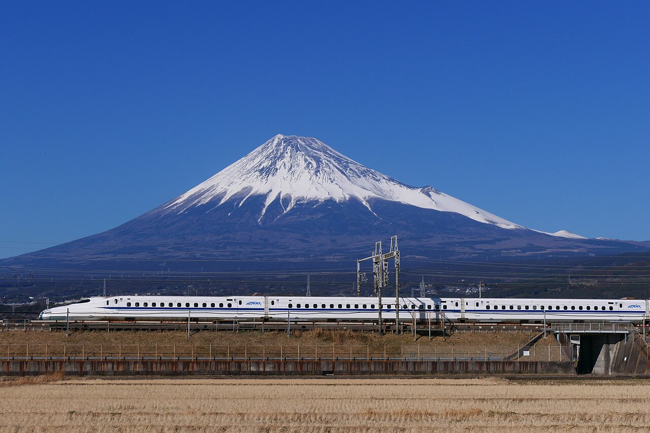 A high-speed commuter train runs in front of a snow-capped mountain.